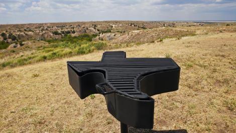 A Texas-shaped barbeque grill with rugged Texas scenery in the background