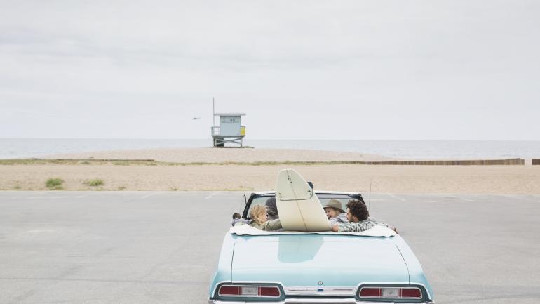 Amigos en un convertible con una tabla de surf llegando a una playa cerca de Los Ángeles, California