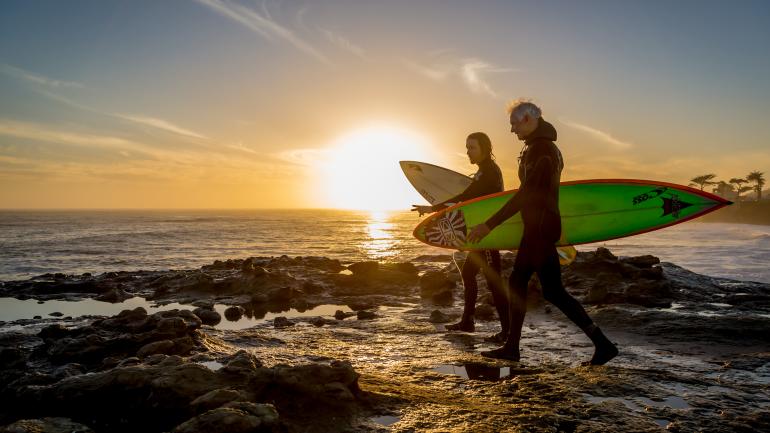 Dos surfistas caminando con sus tablas en Santa Cruz, California, durante la puesta del sol