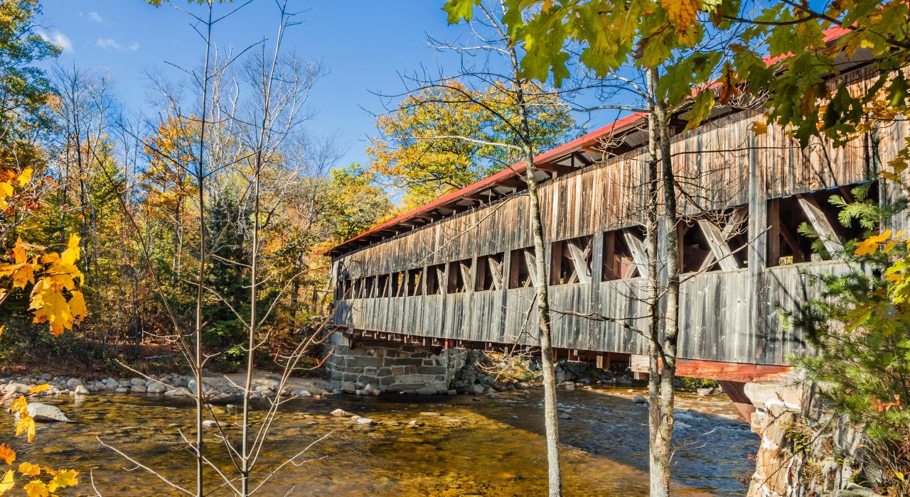 Fall foliage surrounding the covered bridge crossing the Swift River